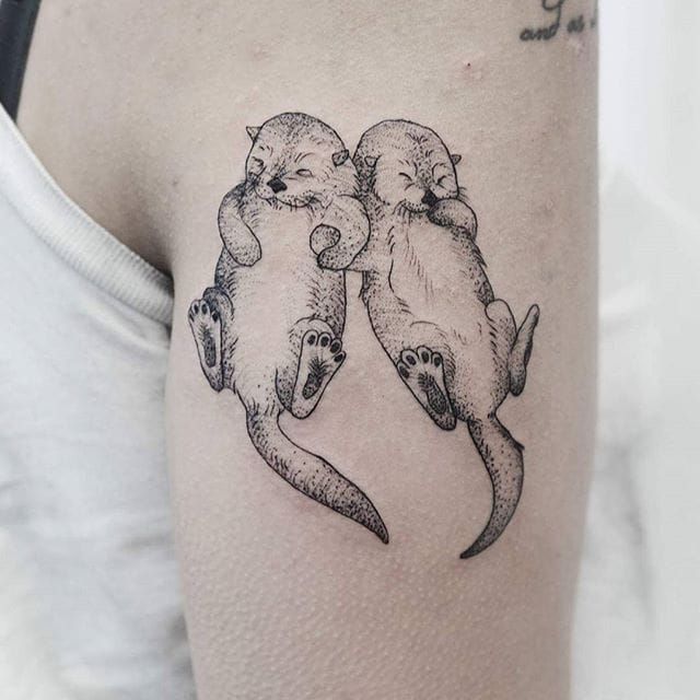 Fine line style otter tattoo located on the bicep