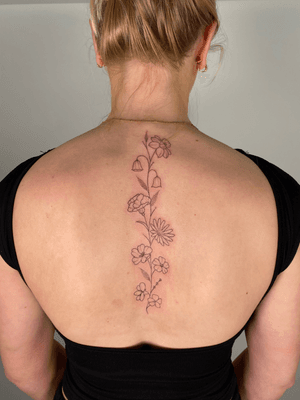 Fine line dotwork tattoo by Chloe Hartland featuring a delicate floral design along the spine.