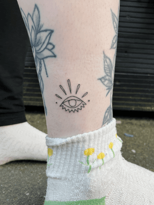 Blackwork evil eye tattoo by Laura, featuring intricate fine line hand poked details for a powerful and unique look.