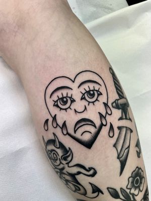 Illustrative tattoo of a heart with a sad face, by tattoo artist Marc 'Cappi' Caplen, combining classic style with emotive symbolism.