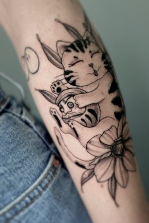 Illustrative black and gray tattoo featuring a cat and daruma design, in traditional Japanese style with dotwork details, by artist Andrea.