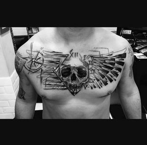 A stunning black and gray tattoo of a skull with wings on the chest, expertly done by tattoo artist Sandro Secchin.