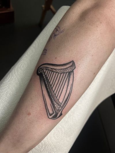 Illustrative black and gray tattoo depicting a detailed harp, symbolizing music and harmony, by artist Claudia Vicente.