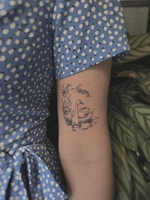 Immerse yourself in the serene beauty of a fine line, illustrative tattoo featuring a scenic swan on a peaceful lake by the talented artist Alina Amberland.