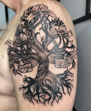 Unique black and gray tattoo featuring an illustrative tree with small lettering on a banner by Alfonso Barberio.
