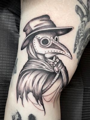 Get a haunting black and gray illustrative tattoo of a plague doctor by Amandine Canata, capturing the mysterious allure of this historical figure. Perfect for those who appreciate dark and intriguing art.