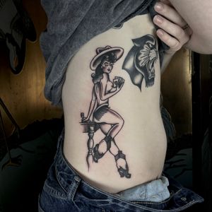 Get a classic illustrative tattoo of a beautiful cowgirl pinup done by the talented artist Marc 'Cappi' Caplen.