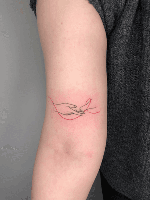 Illustrative fine line tattoo by Winnie Shwe featuring a woman's hand with a cat paw connected by a red thread symbolizing fate.