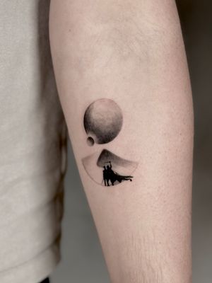 Captivating black and gray tattoo featuring a moon and planet rising over a dune-filled desert landscape, by the talented Saka Tattoo.