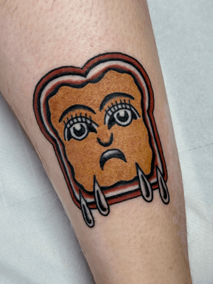 An illustrative traditional tattoo by Jakob Isaac featuring a sad face surrounded by bread and butter elements.