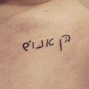 "HUMAN" written in cursive Hebrew, in the client's handwriting, on the client's left collarbone