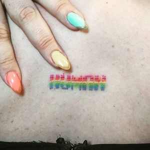 Custom pixelated HUMAN tattoo in rainbow colours in the middle of the client's back.