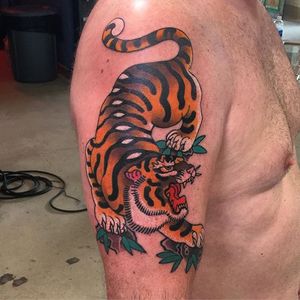 Get an amazing Japanese tattoo by the renowned artist Ami James. This design features a fierce tiger and beautiful flower, perfect for your upper arm.
