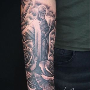 Capture the beauty of London with a black and gray illustrative tattoo featuring a flower and Christ statue on your forearm. Book your appointment in London, GB today!