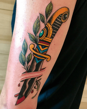 A striking traditional dagger tattoo on the forearm, featuring blood splatter and leaf details. Created by renowned artist Darren Brass.
