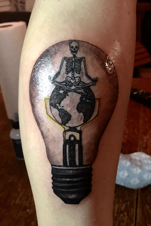 Clients design.  Tiny meditating skeleton on world in a light bulb. Side of calf 