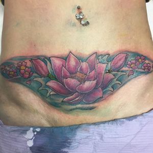 Cover up de cicatrices de césarienne. Lotus et fleurs de cerisier dans l'eau avec des vagues. Tatouage sur le bas du ventre d'une femme. Lotus néotrad Lotus néo traditionnel.