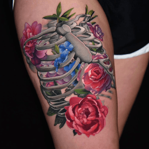 Realistic ribcage tattoo on the thigh, intertwined with colorful flowers. 