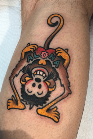 Get a unique leg tattoo of a monkey with aloha lettering, designed by artist Felipe Reinoso in a traditional style.