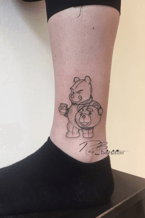 Unique blackwork illustration of Pooh Bear wearing a mask, surrounded by honey, on lower leg by Patrick Bates.