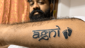 Agni - Name of fire in Sanskrit. By naming his daughter as Agni, he is transferring the power and purity of fire. Showing his love towards his daughter by placing the script on his hand and heart