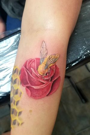 A tattoo of a fuzzy bee burying his head in the middle of a red rose.