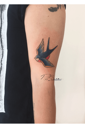 Get a timeless illustrative bird tattoo on your upper arm by the talented artist Patrick Bates. Embrace the classic style with this stunning design.