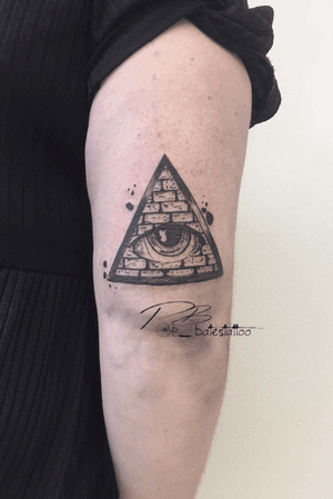 Black and illustrative upper arm tattoo featuring a triangle, eye, and brick wall motif by Patrick Bates.