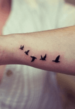 Small size flock of birds flying on underside of wrist in black silhouettes.