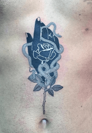 Inverted color traditional/illustrative black and white snake wrapped around a hand and rose design on clients stomach from sternum to belly button.