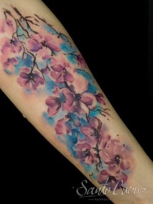 Vibrant cherry blossom design on forearm by artist Alex Santo, beautifully blending watercolor technique with floral motif.