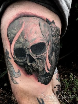 This black and gray tattoo featuring a skull is expertly done by tattoo artist Alex Santo on the upper leg for a striking and eerie look.
