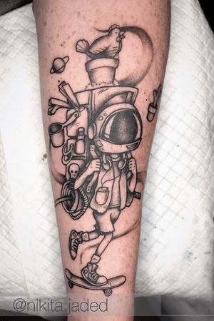 Explore the galaxy with this blackwork forearm tattoo featuring a moon, planet, astronaut, bird, skull, helmet, and backpack. By Nikita Jade Morgan.