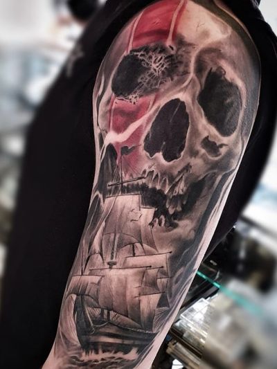 Get a bold black and gray trashpolka tattoo of a skull and ship by Mauro Imperatori on your upper arm for a fierce and edgy look.