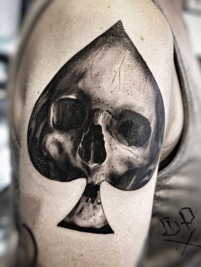 Bold blackwork tattoo featuring a skull and card design on the upper arm, created by renowned artist Mauro Imperatori.