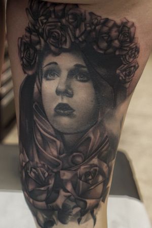 Stunning upper leg tattoo by Phillip Wolves, featuring a detailed black and gray illustration of a beautiful woman and delicate flowers.