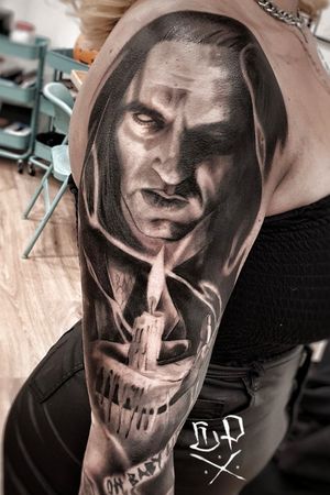 Capture the dark beauty of a vampire next to a flickering candle in this striking black and gray upper arm tattoo by Mauro Imperatori.