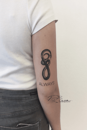 Patrick Bates creates a bold blackwork tattoo combining a snake motif with fine line illustrative lettering on the upper arm.
