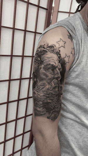 Impressive black and gray realism tattoo of a bearded man resembling Zeus, by Alejandro Gonzalez.