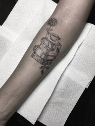 Get inked with a beautiful black and gray tattoo featuring a flower, coffee cup, and book design, by the talented Alejandro Gonzalez. Perfect for book and coffee lovers!