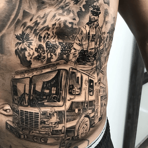 Detailed black and gray illustration on ribs featuring an axe, truck, firefighter, fire, and flames by artist Jake Masri.