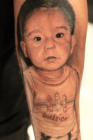 A stunning black and gray tattoo of a child's portrait on the forearm, expertly done by artist Jake Masri.