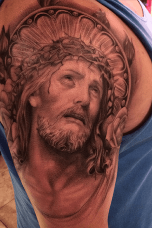 A striking black and gray tattoo of Jesus, featuring thorns, blood, and a beard on the upper arm. Expertly executed by tattoo artist Jake Masri.