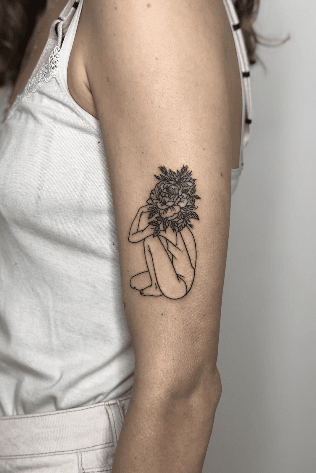 Fine line flower head woman tattoo on the tricep