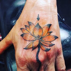 This lotus flower hand tattoo with a stem going down the middle finger