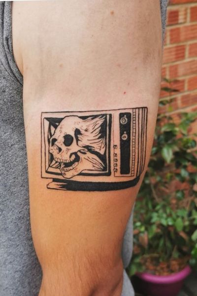 Get a bold and colorful new school tattoo featuring a skull and TV motif on your upper arm, expertly done by Jonathan Glick.