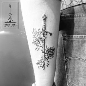Elegant forearm tattoo featuring a delicate flower intertwined with a sword, done by Chasinghawk Tattoos.