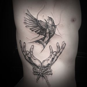 Detailed black and gray sketchwork tattoo of a bird and hand design on the ribs, by Aygul.