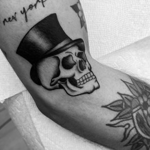 Blackwork illustrative tattoo by Miss Vampira featuring a skull wearing a hat, on the arm.