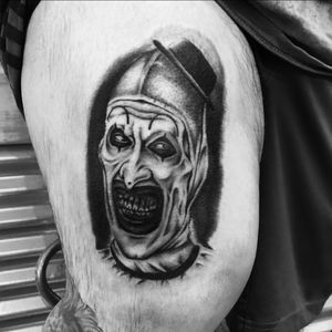 Get a striking blackwork horror tattoo of a sinister clown with hat by the talented Miss Vampira on your upper leg.